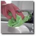 Unterhaltsreinigung - Büroreinigung - Reinigungskraft mit Gummihandschuh und Mikrofasertuch reinigt eine Sanitärarmatur.