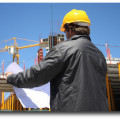 Baureinigung - Bauschlussreinigung - Bauendreinigung - Baufeinreinigung - Endreinigung - Schlussreinigung - Feinreinigung - Ein Bauarbeiter betrachtet Baupläne auf einer Baustelle.